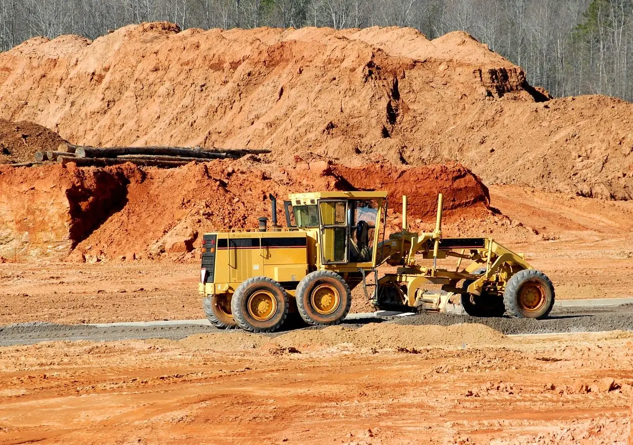 Yellow motor grader working beside a tall bank of red earth